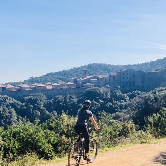 Cycliste sur un sentier en terre avec la vue au loin de la Chartreuse de la Verne posée au milieu de la forêt des Maures Cycliste sur un sentier en terre avec la vue au loin de la Chartreuse de la Verne posée au milieu de la forêt des Maures