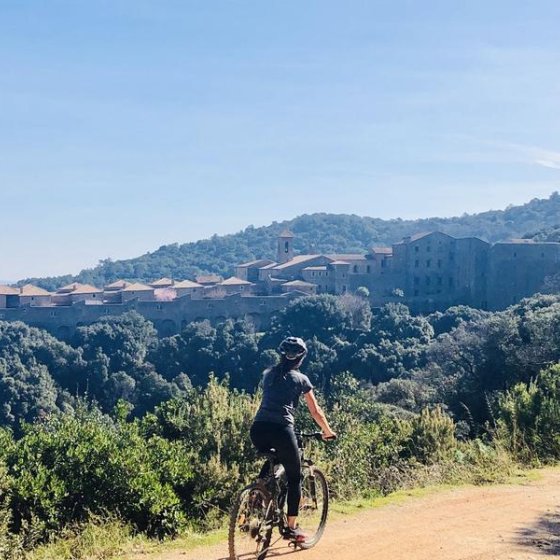 Cycliste sur un sentier en terre avec la vue au loin de la Chartreuse de la Verne posée au milieu de la forêt des Maures